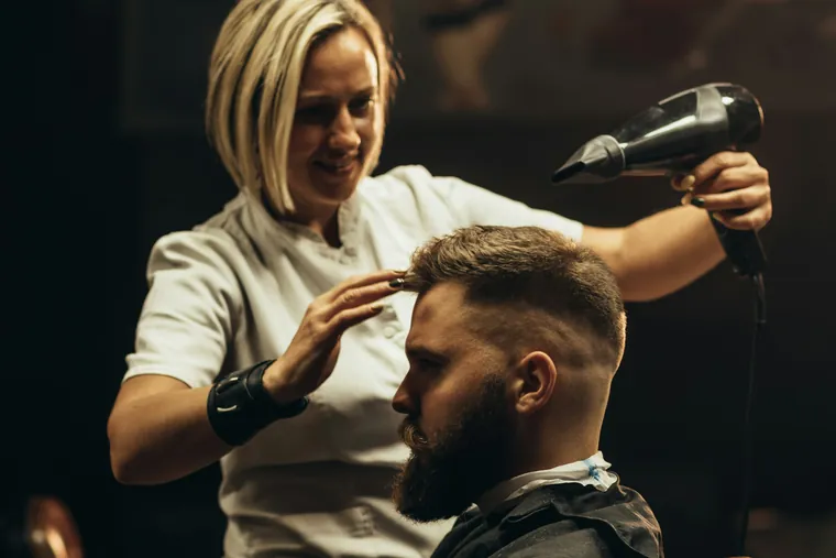 Barbière séchant la barbe d’un client dans un salon sombre