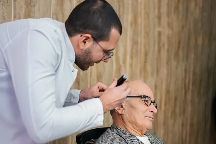 Coiffeur coupant les cheveux d’un client âgé installé chez lui